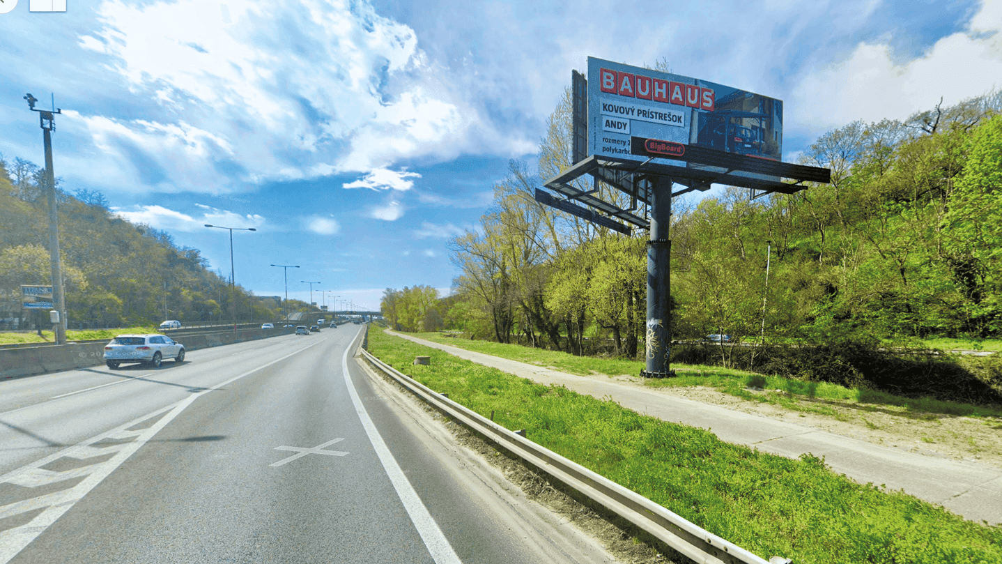 Záber na predchádzajúcu podobu vjazdu na Most Lanfranconi v smere do Petržalky s veľkou reklamnou plochou na stĺpe vedľa chodníka a cesty.